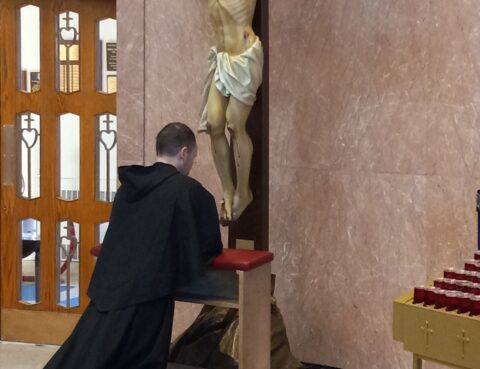 A friar on pilgrimage kneeling before the crucifix